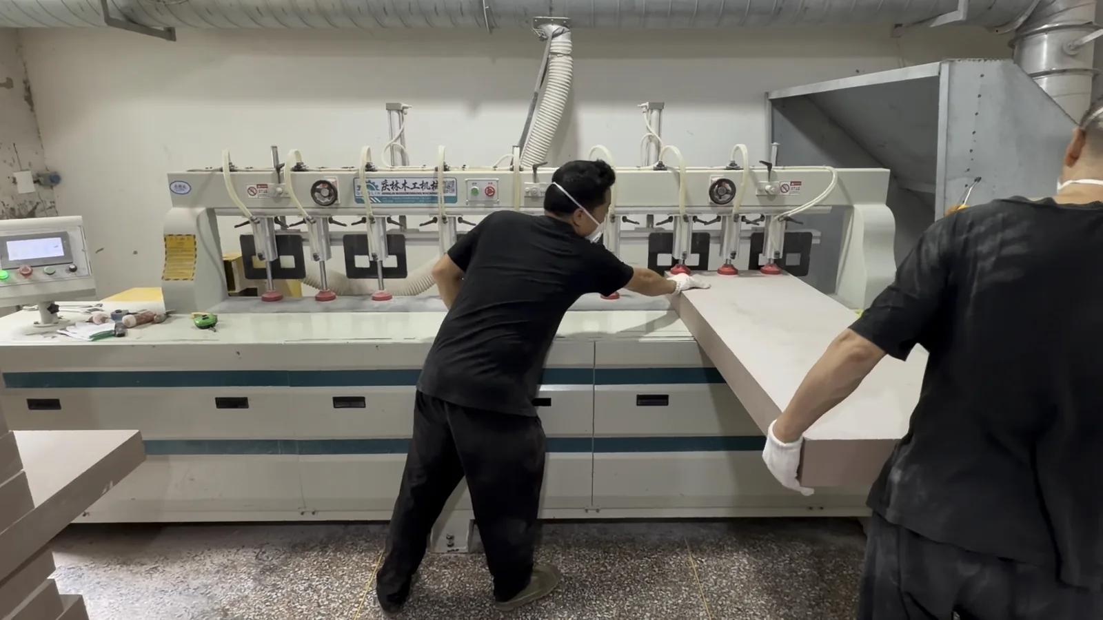 Two operators handling a tooling board beside material preparation equipment