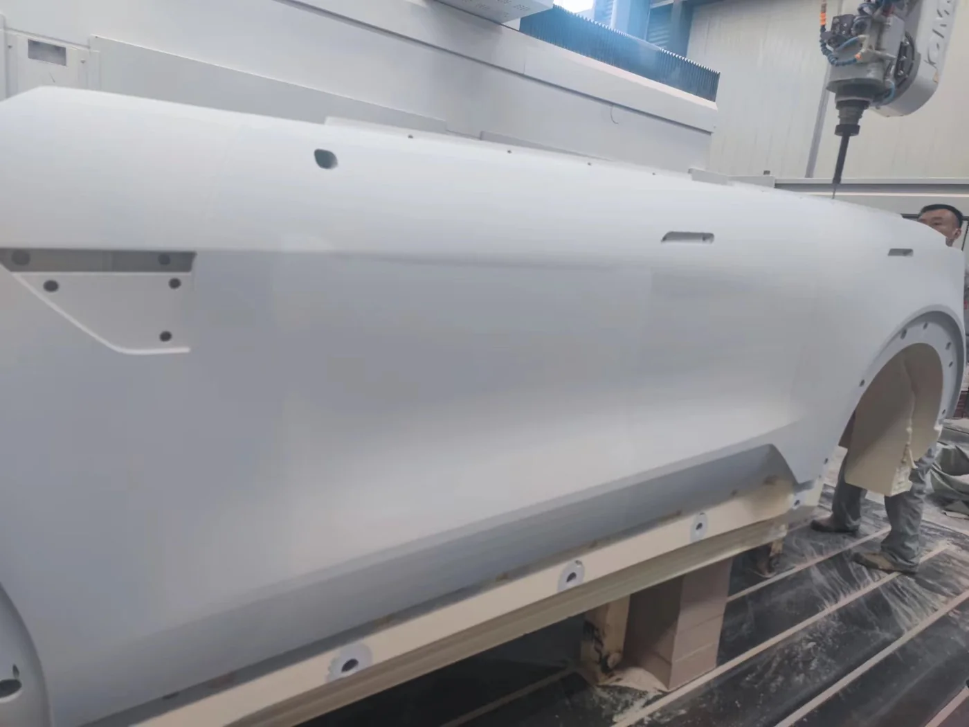 A white vehicle body model beside machining equipment